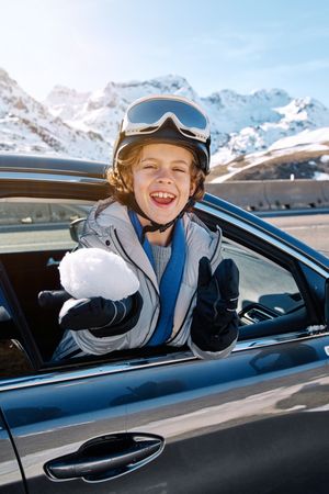 Joyful boy with snowball riding in car