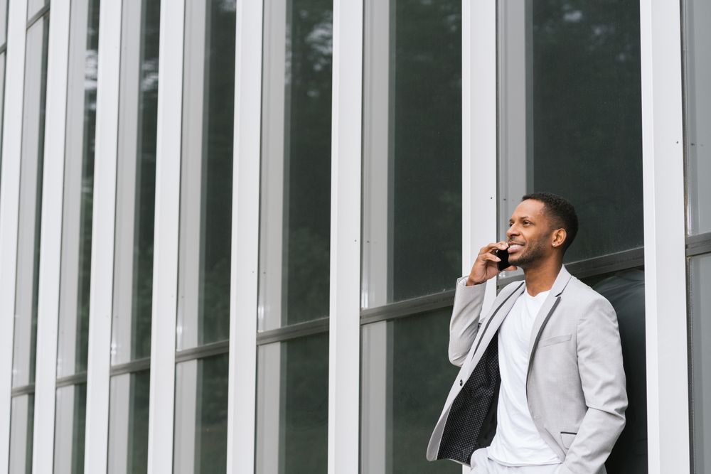 Elegant Black man talking smartphone leaning building