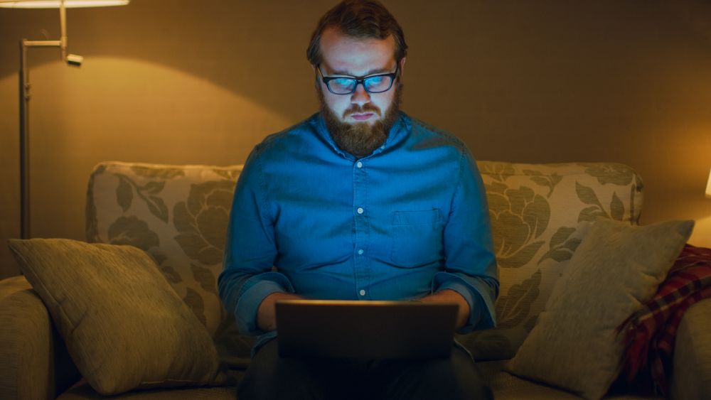 Portrait Shot of a Man Sitting on a Couch in His Living Room, Laptop on His Knees.