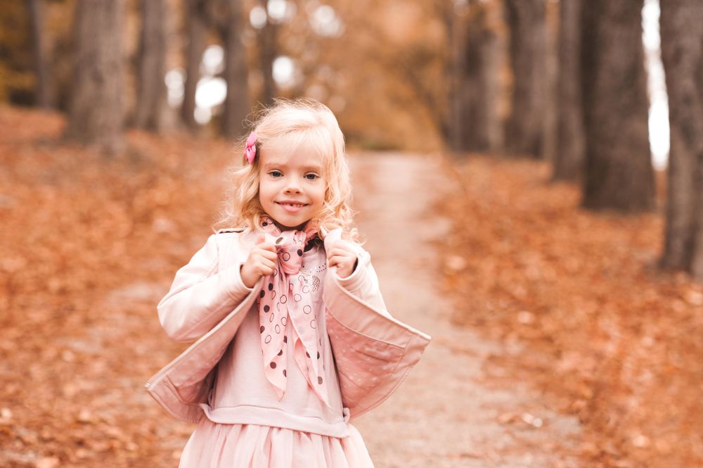 Young girl wearing pink jacket standing on brown tree leaves