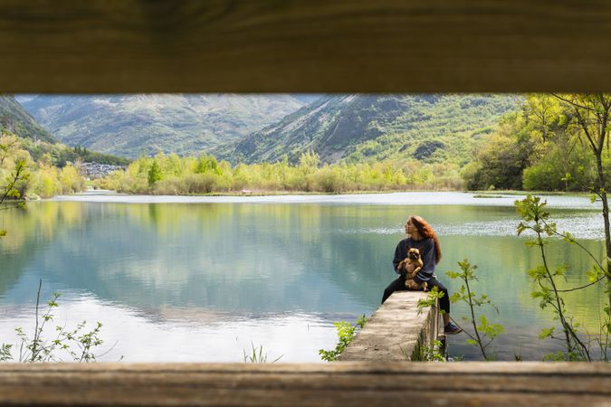 Traveling woman with dog on pier near lake in mountains