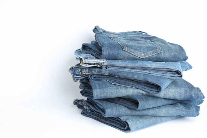 Stack of jeans pants on light background, space for text