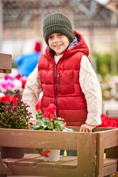 Adorable boy leaning on wooden garden cart with flowers