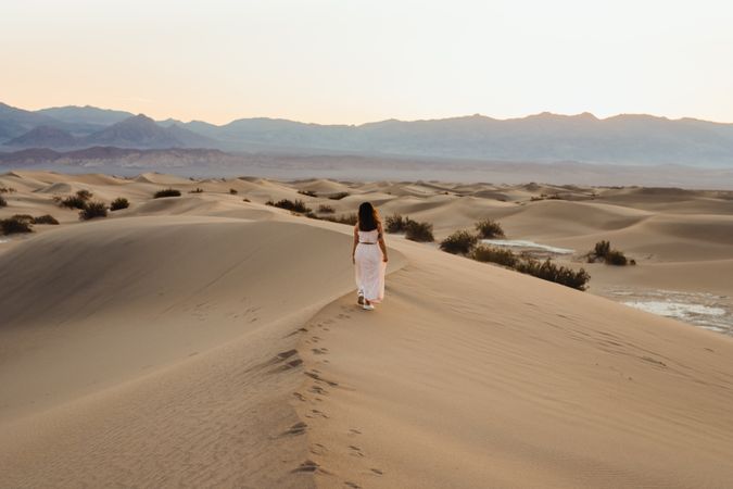 Back view of young woman walking in desert leaving footprints in dry sandy dunes in Death Valley