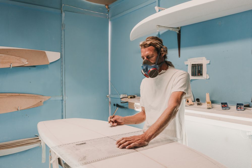 Man in respirator measuring surf board in workshop