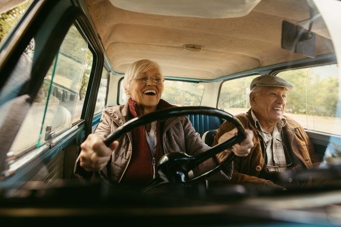Woman with gray hair driving car with her partner enjoying the ride and laughing