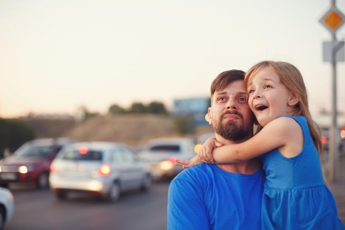 Female child and father standing with cars in background