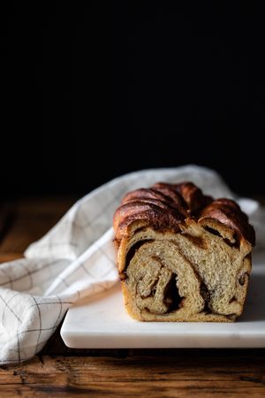 Fresh twisted bread or cinnamon babka over wooden table with striped towel on blurred background
