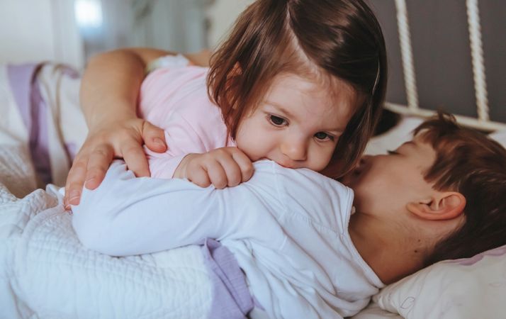 Close up of adorable little girl playing over brother lying in the bed