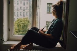 Interested woman reading book at window sill at home