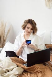 Woman Sitting In Bed Spending Time In Bedroom With Phone