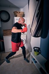 Man training boxing in the laundry room at home with a bag