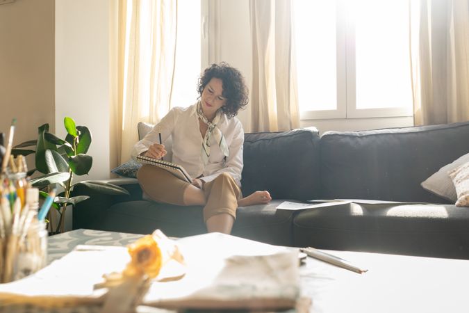 Woman writing on paper on sofa in room