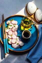 Top view of sliced radishes on blue plate served with oil and chopsticks