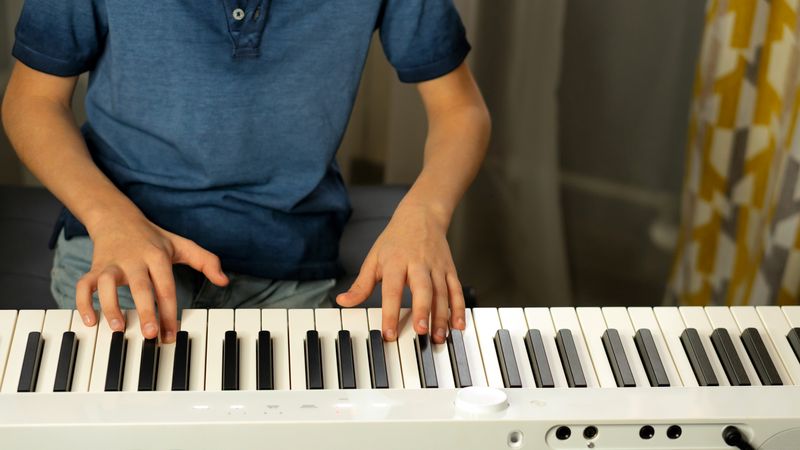 Close-up of child's hands playing white digital piano