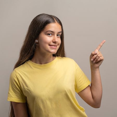 Smiling young woman pointing her index finger up to an empty copy space.