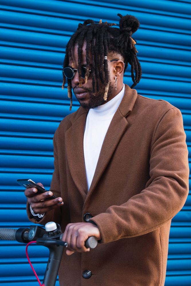 Stylish Black man with electric scooter using smartphone