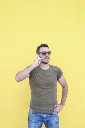 Male standing in front of yellow wall talking on smartphone