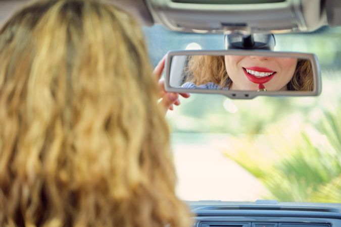 Smiling woman applying red lipstick in car front seat