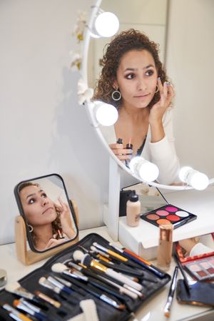Young positive woman applying makeup of liquid blush on cheeks