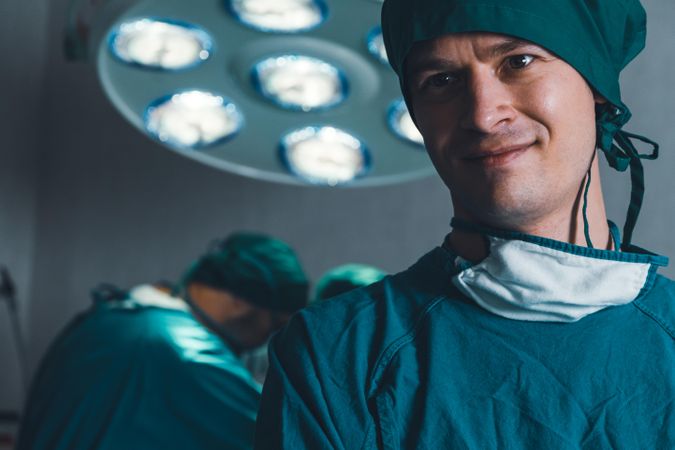 Male doctor in operating scrubs with surgery happening in background