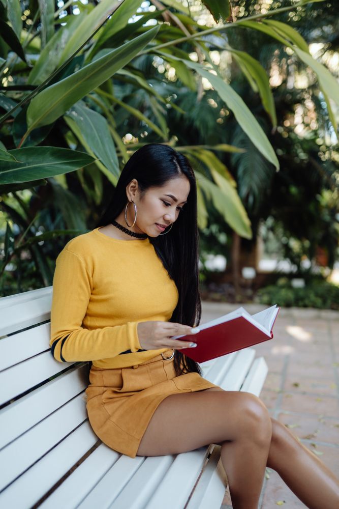 Graceful long haired Asian woman reading book on bench in park