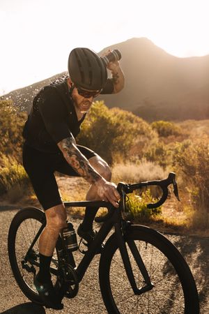 Racer cooling himself with water while riding a bicycle on open road
