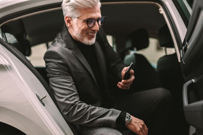 Smiling mature businessman sitting in the backseat of a taxi and looking at his phone