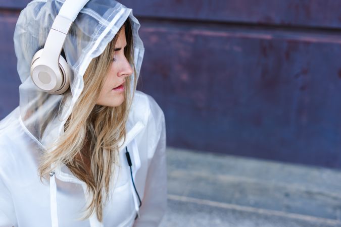 Pensive stylish woman in raincoat with headphones