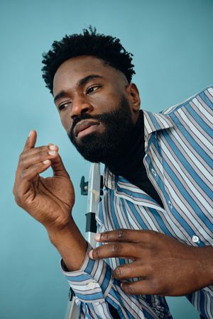 Black male model in striped blue shirt and jeans posing in blue studio