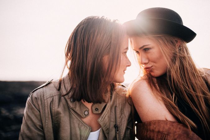 Two young women leaning into each other face to face playfully outside