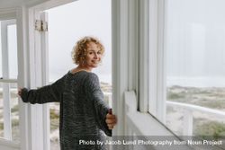 Side view of a woman standing at the door looking at the beach 5Q2Bgn
