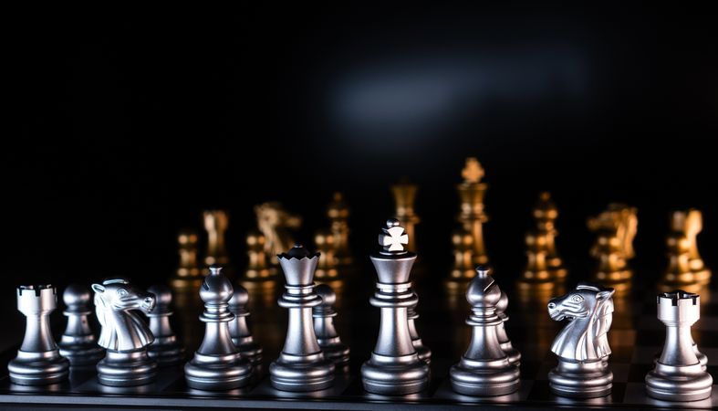 Silver and golden chess pieces on reflective board.