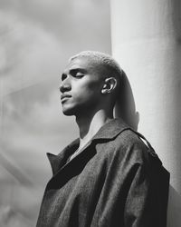 Monochrome side view shot of stylish young man leaning against column