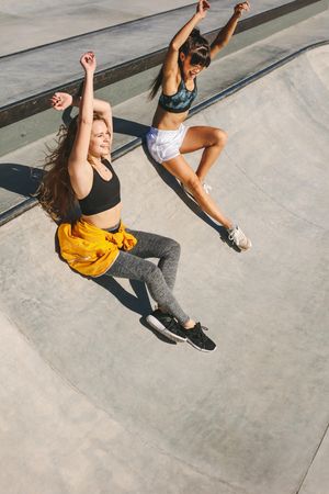 Two smiling friends sliding down from skating bowl