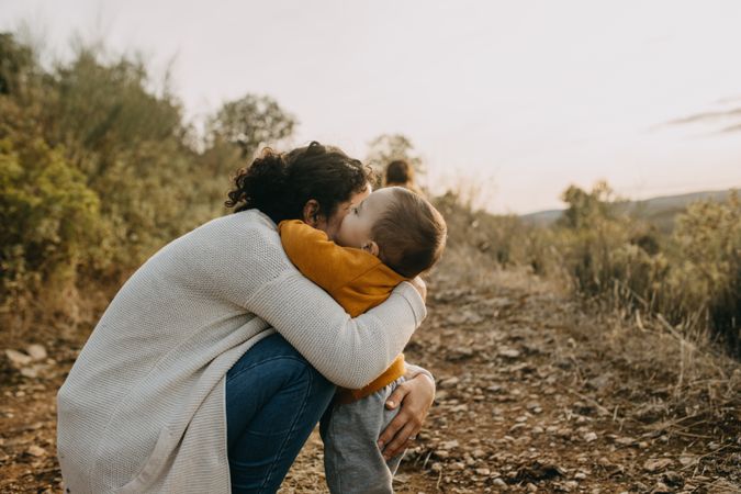 Mother sitting and hugging her baby boy on a walking trail outside
