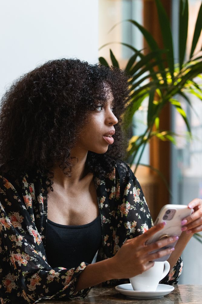 Black woman using smartphone at table with hot drink