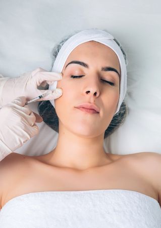 Aesthetician's hand's in latex gloves injecting filler into female's cheek in a beauty salon