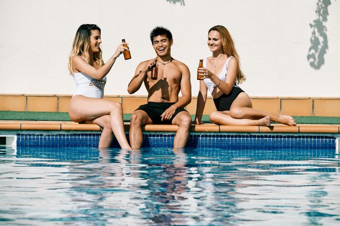 two young women and an asiatic man drinking beer by the pool