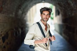 Portrait of dark haired man standing within arch of city street