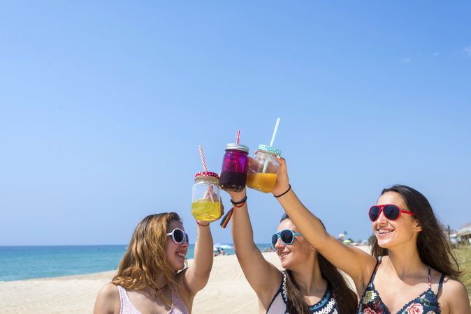 Group of happy female friends toasting non alcoholic drinks on summer beach