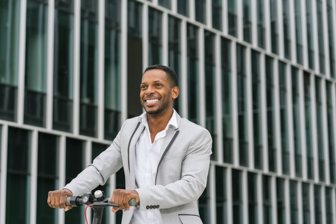 Black man in suit on electric scooter in business center