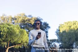 Smiling Black male with sunglasses standing in park holding phone 41l1v8