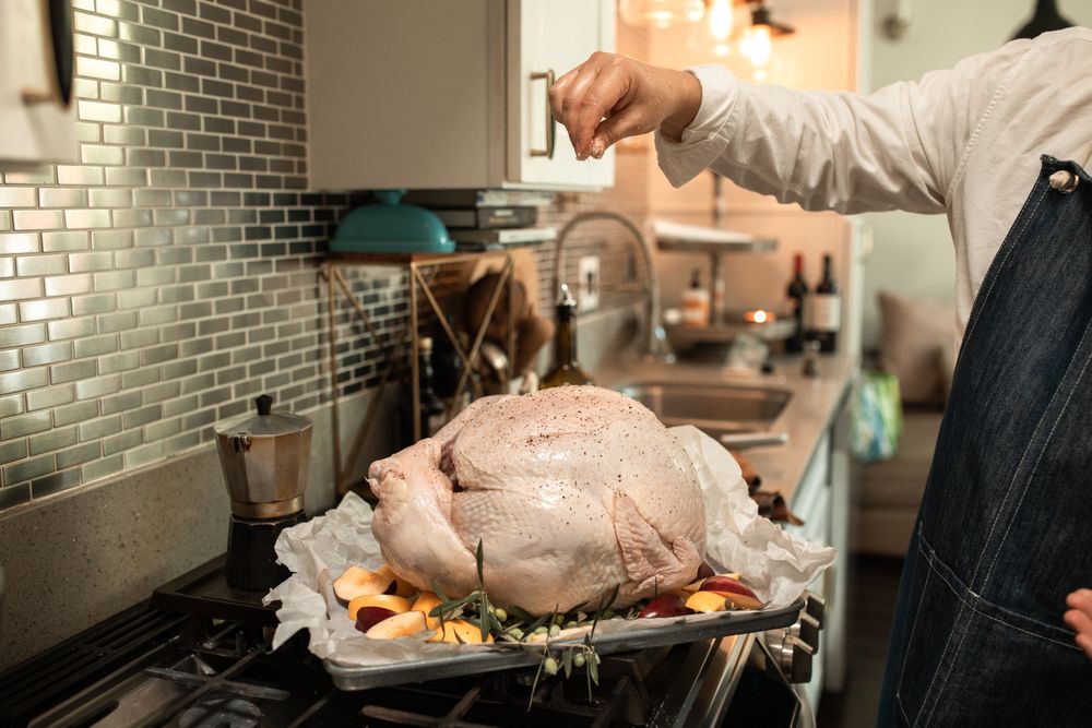 Chef wearing an apron adding a sprinkle of herbs over uncooked turkey