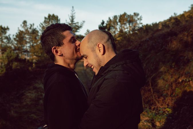 Smiling men hugging and kissing on countryside road