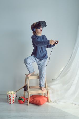 Preteen boy in virtual reality glasses and headphones using joys