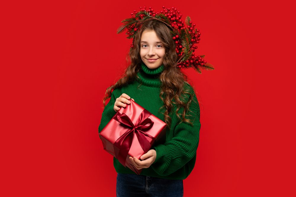 Young girl in green sweater holding wrapped red gift