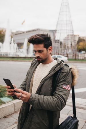 Young male in warm jacket using smartphone