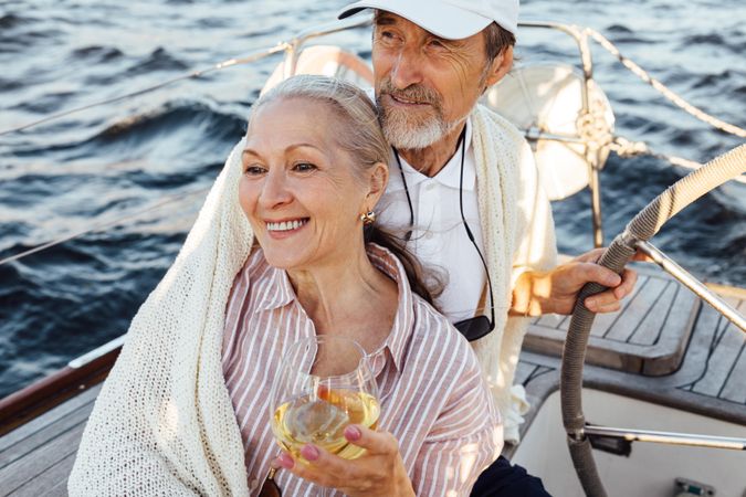 Happy older woman with wine being held by her partner on a boat