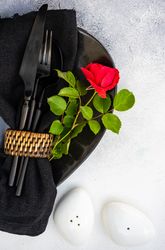 Top view of dark table setting with red rose